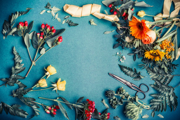 Various autumn flowers and leaves arrangement with shears for decoration bouquet making on blue...