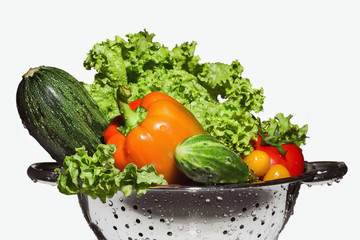 A metal colander with colorful vegetables on white and copy space.