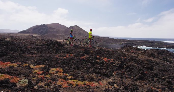 Mountain biking MTB cyclist woman and man resting while cycling on bike trail. Mountain biker couple riding bicycle enjoying healthy active lifestyle in nature, Lanzarote, Canary Islands, Spain