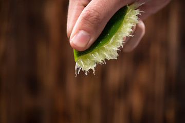 Hand squeeze lime with lime drop on dark wooden background