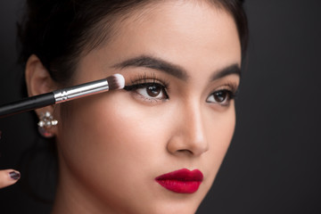 Close up of hand of asian woman applying eyeshadow on female eyelid.