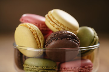 assorted macarons in glass bowl on wood table, closeup