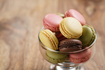 assorted macarons in glass bowl on wood table, closeup