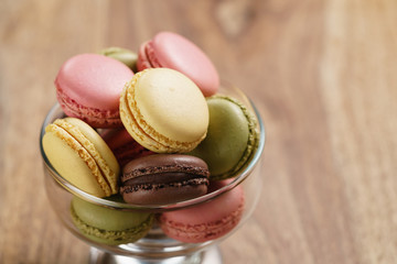 assorted macarons in glass bowl on wood table, closeup