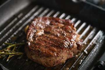 beef rib eye steak with rosemary on grill pan closeup, shallow focus