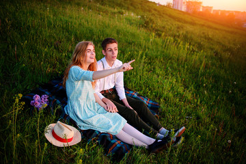 young couple sitting on the plaid in the park and look at the sunset