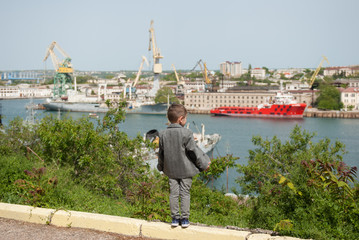 Fototapeta premium little boy in a jacket stands against the background of a seaport