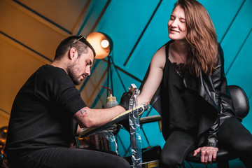 master tattooist makes a tattoo on the skin of the hand client girl in a workshop with special...
