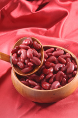 red kidney beans in wooden bowl and wooden spoon on red background