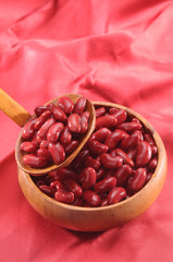 red kidney beans in wooden bowl and wooden spoon on red background