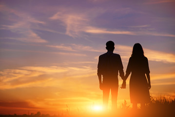 young couple is holding hands on a background sunset silhouette © cezarksv