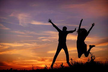 A young man with his girlfriend jump on background sunset silhouette.