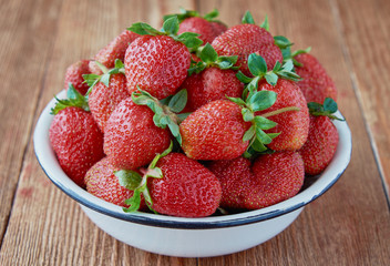 Delicious red sweet fresh strawberry in a white bowl on a wooden background.