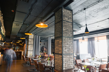 Hall semi-éclairé de style loft dans un restaurant mexicain avec cuisine ouverte en arrière-plan. Devant la cuisine, il y a des tables en bois avec des chaises et des canapés multicolores. Sur les canapés là