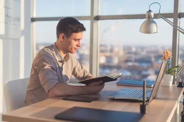 Man working in modern office, writing down new ideas his notebook, searching information using portable computer at workplace