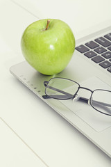 green apple and eye glasses on laptop computer. healthy eating in office life