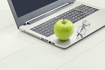 green apple and eye glasses on laptop computer. healthy eating in office life