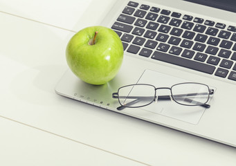 green apple and eye glasses on laptop computer. healthy eating in office life