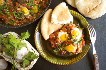 Shakshouka with pita bread on the pan. In the middle East, a traditional dish. Scrambled eggs with tomatoes, peppers, vegetables and herbs. Shakshuka on the table. The view from the top.