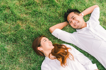 Young Asian lovely couple or college students lying down on the grass together, listening to music, top view with copy space. Love, relationship, wedding, or relaxing casual lifestyle concept