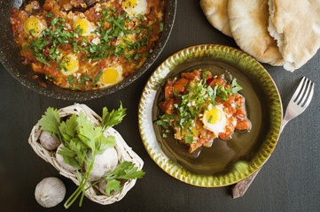 Shakshouka with pita bread on the pan. In the middle East, a traditional dish. Scrambled eggs with tomatoes, peppers, vegetables and herbs. Shakshuka on the table. The view from the top.