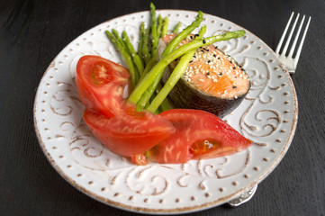 Asparagus with salmon on a white plate. On a black background.