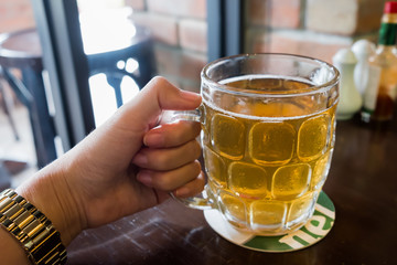 A lady's hand holding a pint glass of local beer on the wooden table