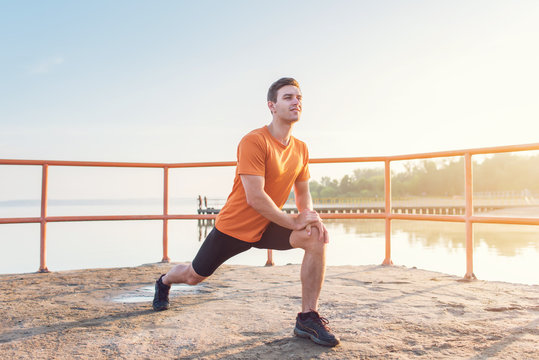 Young fit man stretching legs outdoors doing forward lunge.