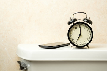 Naklejka premium black vintage alarm clock with smartphone on toilet tank in the morning