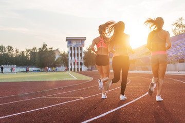 Rear view of women athletes running together in stadium.