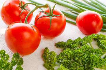 Fresh juicy tomatoes, parsley and greens on a light wooden background concept of health and vegetarian food