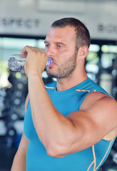 Fototapeta na wymiar Resting time. Handsome young men in sports wear wearing towel on his shoulders and holding water bottle while sitting at gym