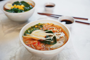 Ceramic bowl of traditional asian ramen soup with noodles, spring onion, chicken, sliced egg and mushrooms served with wooden chopsticks on white table. Selective focus.