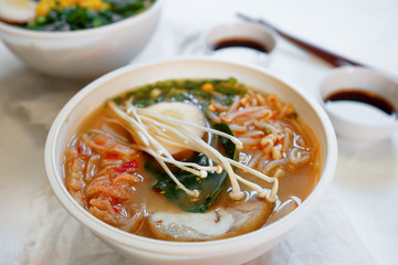 Ceramic bowl of traditional asian ramen soup with noodles, spring onion, chicken, sliced egg and mushrooms served with wooden chopsticks on white table. Selective focus.