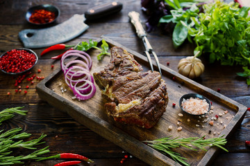 Roasted meat  with onions, garlic, spices, fresh herbs, red pepper and salt on wooden cutting board in rustic style. selective focus, prime beef, slow food concept