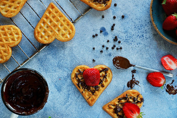 Belgian waffles in the shape of hearts with fresh strawberries and chocolate topping on blue table. Homemade healthy breakfast, top view