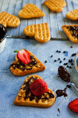 Belgian waffles in the shape of hearts with fresh strawberries and chocolate topping on blue table. Homemade healthy breakfast, selective focus