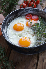 Fried eggs in a frying pan with herbs, cherry tomatoes, bread, olive oil and spices on rustic wooden background. Healthy breakfast,  selective focus