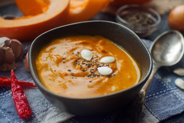 Traditional homemade pumpkin soup with seads, cream and vegetables on dark stone table, healthy eating, autumn harvest, selective focus