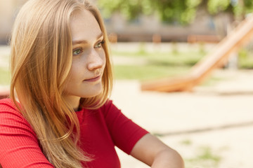 Fototapeta premium Sideways portrait of pretty young student girl with fair hair, charming eyes and freckles looking pensively into distance thinking over her future project isolated over playground. People, lifestyle