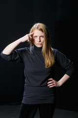 Young blonde hair girl raised her finger to her head against a black background