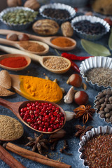 Various indian spices in wooden spoons and metal bowls, herbs and nuts on dark stone table. Colorful spices, selective focus. Healthy food background