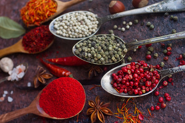 Various indian spices in wooden and silver spoons and metal bowls, seeds, herbs and nuts on dark stone table. Colorful spices, selective focus. Organic food, healthy lifestyle.