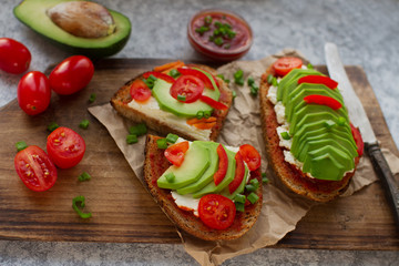 Organic homemade avocado toasts on rye bread with tomatoes, scallions, pepper and cream cheese on vintage wooden board, selective focus. Healthy eating concept