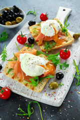 Fototapeta na wymiar Poached egg on grilled toast with smoked salmon, rucola, olives and vegetables on white board. healthy breakfast