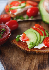 Organic homemade avocado toasts on rye bread with tomatoes, scallions, pepper and cream cheese on vintage wooden board, selective focus. Healthy eating concept
