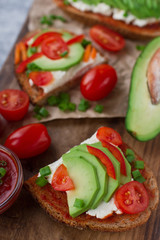 Fototapeta na wymiar Organic homemade avocado toasts on rye bread with tomatoes, scallions, pepper and cream cheese on vintage wooden board, selective focus. Healthy eating concept