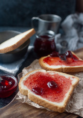 Homemade toasts with strawberry jam on wooden board, craft paper and dark stone background. Delicious breakfast,  selective focus,  
