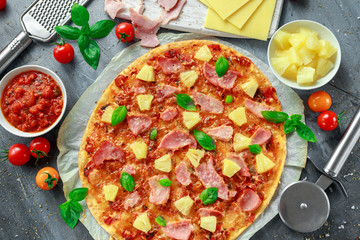 Fresh baked pizza hawaii with ham and pineapple, basil, tomatoes on backed paper