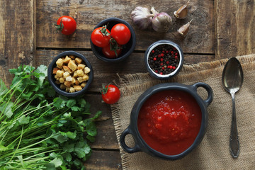 tomato soup with fresh herbs, clove, black pepper and crackers on rustic wooden background, top view.